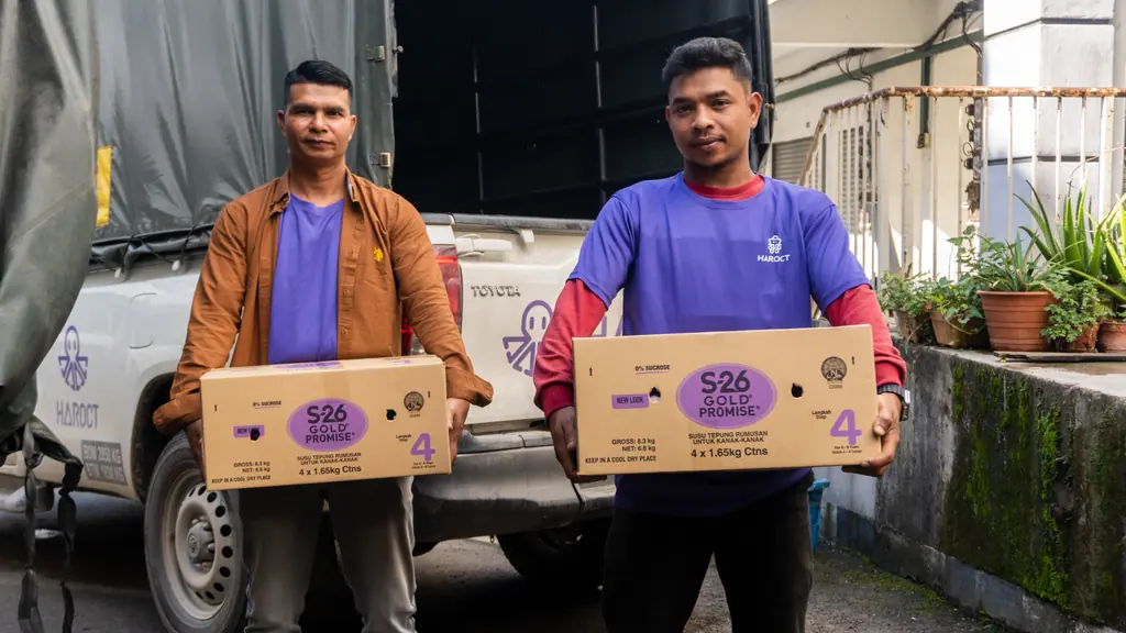 Two Haroct staff carrying cartons of produce next to a pickup truck