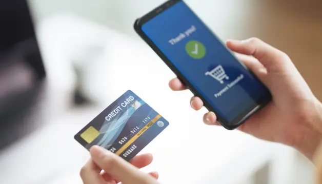 A hand holding a phone showing a successful payment, with a credit card in the other hand
